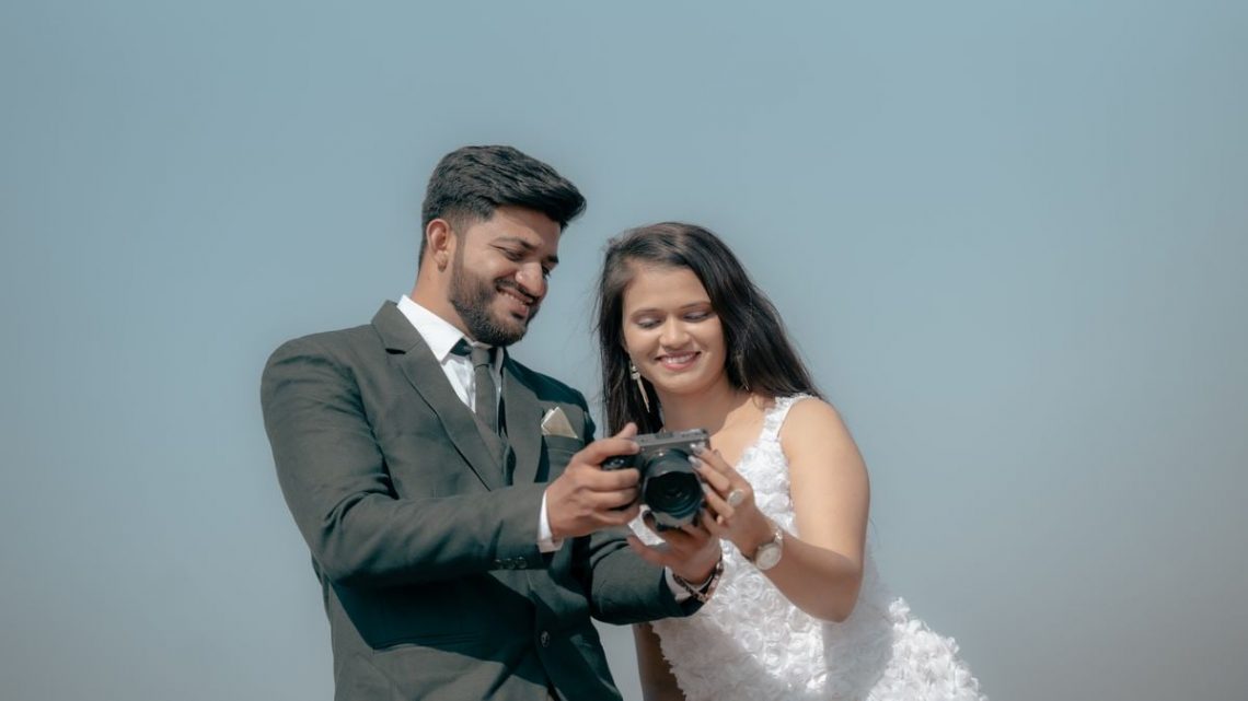 Smiling couple reviewing photos on camera during an outdoor pre-wedding shoot.